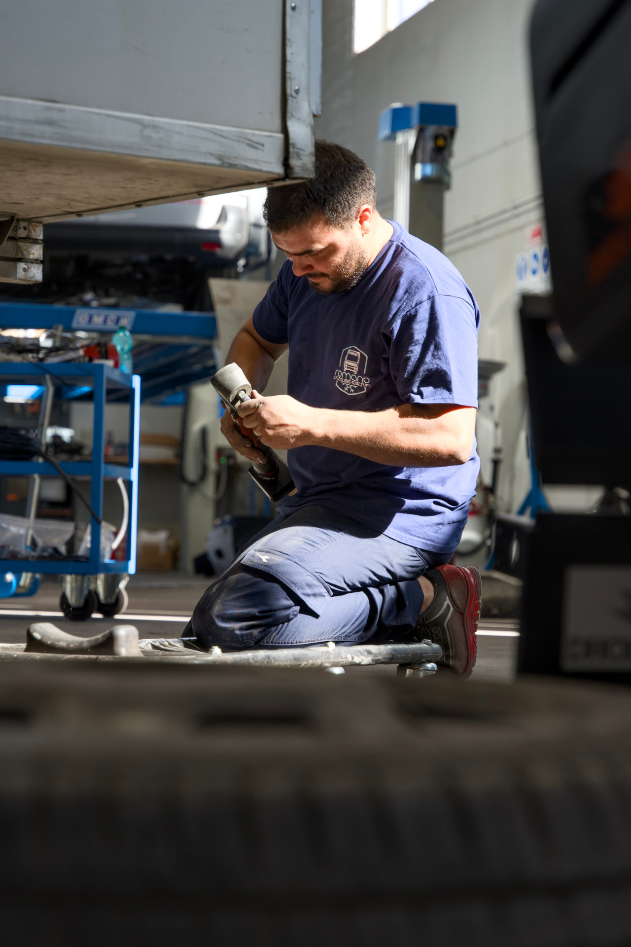 Tecnico al lavoro sotto un veicolo refrigerato con avvitatore in officina